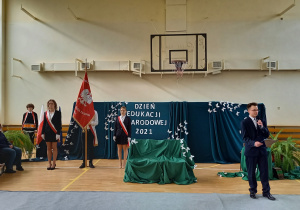 poczet sztandarowy liceum i konferansjer na tle dekoracji podczas uroczystości święta Edukacji Narodowej